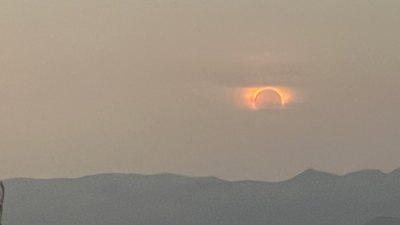 The eclipsed sun as a thin orange arc just above a ridgeline at dusk